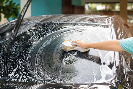 Woman washing windshield with sponge on a black car wash at home.