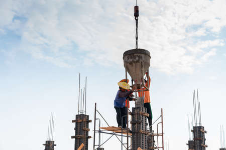 Worker pouring cement pouring into pillars formwork at building area in construction site.