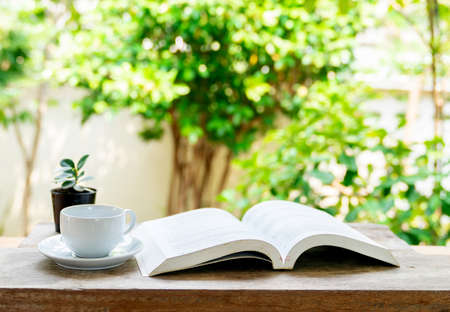 Cup of coffee and opened book on wooden table in front yard. Relax time in holiday.の写真素材
