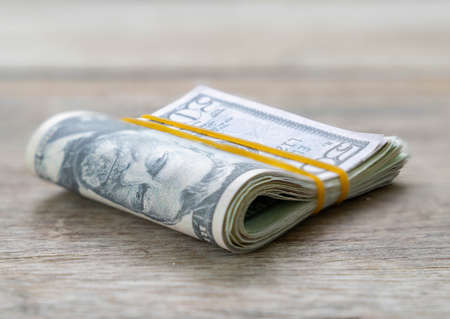 Dollar bills folded and tied with yellow rubber band paste on wooden table.の写真素材