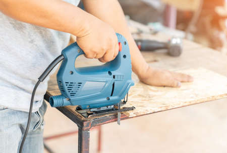 The carpenter use electric jigsaw to cut wood sheet for d.i.y table in holiday.の写真素材