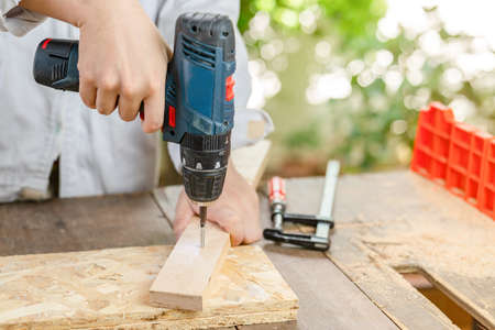 Close up hand hold cordless screwdriver and catch wooden bar on the table and clamp paste on, bokeh background.の写真素材