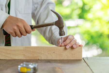 Close up hammering a nail into wooden bar on the table, Bokeh background.の写真素材