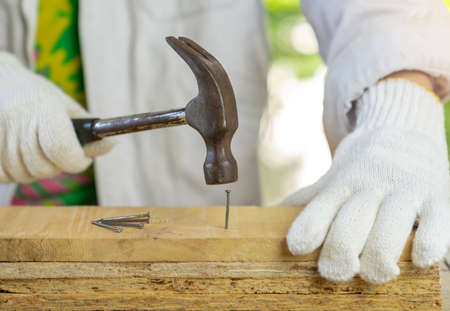 The carpenter ware white gloves hold hammer hit nail on wooden bar, Selective focus.の写真素材