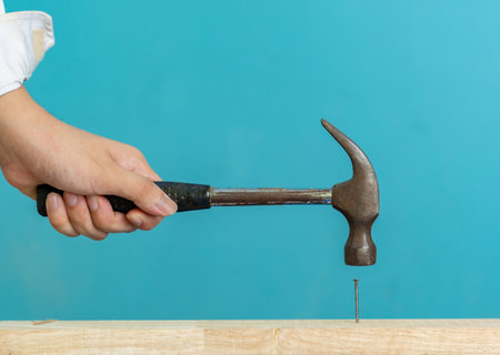 Hand hold hammer hit nail on wooden bar isolate on aqua blue background.の写真素材