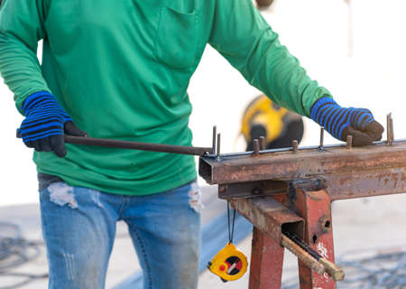 Worker ware gloves bending reinforcement metal rebar rods in construction site.の写真素材