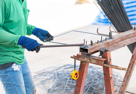 The worker is bending rebars (rods) with gloves and tape measurement in the construction site.