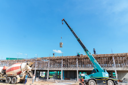 Crane hoist concrete bucket from truck to second floor building in construction site.の写真素材