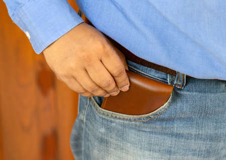 Close-up of a the hand put brown wallet to jeans bag on wood background.