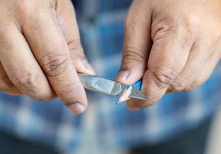 Close up sharpening a pencil with a cutter knife on out of focus background.