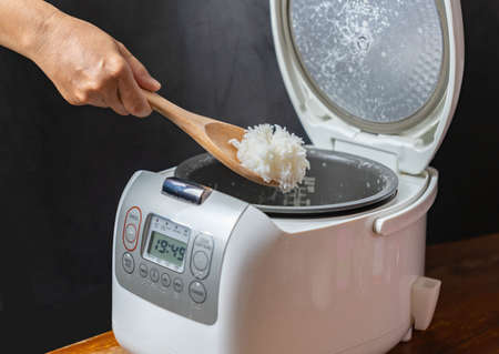 Rice cooking in electric rice cooker and scoop ladle in the kitchen.の写真素材