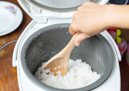 Woman hand use wooden ladle scoop rice in the electric rice cooker.の写真素材
