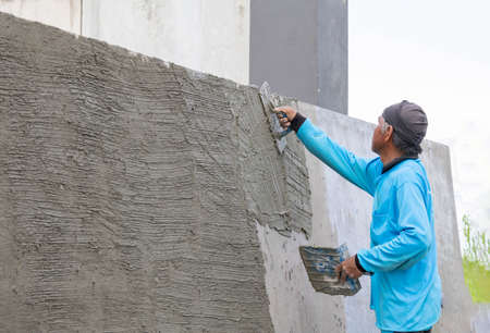 Worker plastering mortar at wall for exposed aggregate finish in construction site.の写真素材