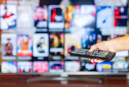 Remote control in hand. smart television in background and content on demand concept.の写真素材