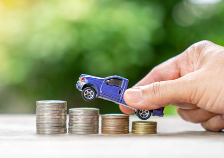 Hand hold blue pickup car model over money coin stack on out of focus background.の写真素材