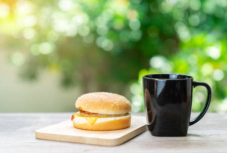 Cheese hamberger on wooden board and coffee in the holiday mornig it's relax time on out of focus tree background.の写真素材