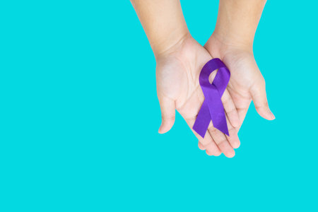 Purple ribbon in two hand on isolate aqua blue background. Concept of world cancer day.の写真素材