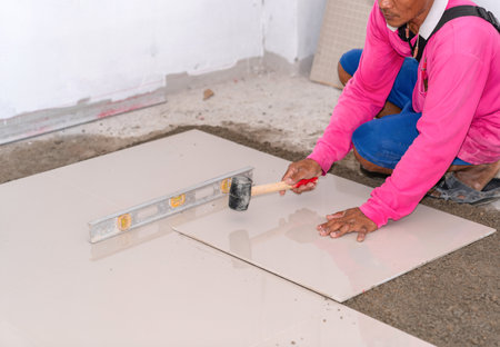 Worker laying the ceramic tile on the floor and knock for smooth floor in building site.の写真素材