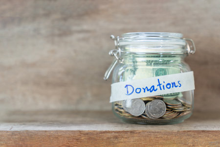 Close up Coins in glass jar for giving and donation concept on wooden table.の写真素材
