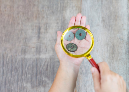 Magnify glass zoom collectible coins and a hand on wooden table.の写真素材