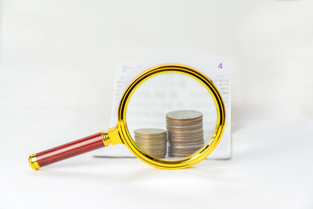 Magnifying glass focus on stack of coins and book bank concept of saving and interest.の写真素材