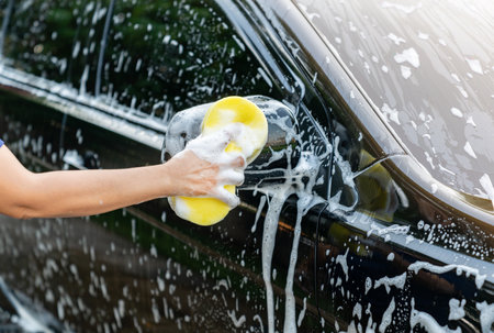 Woman washing black car with sponge on her house. Car detailing.の写真素材