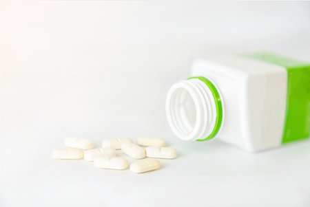 White pills falling from bottle on white backgroundの写真素材