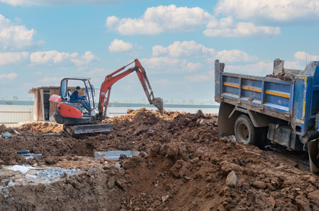 Excavator digging a drain load to truck in front of a construction buildingの写真素材