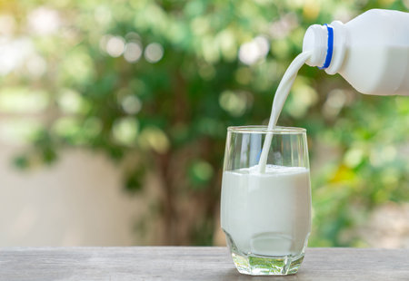 Milk from bottle pouring into glass on out of focus background.の写真素材