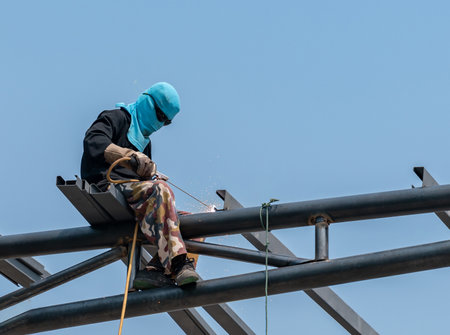 A welder is welding steel on a steel roof truss. Working at height without fall arrestor device in construction site.の写真素材