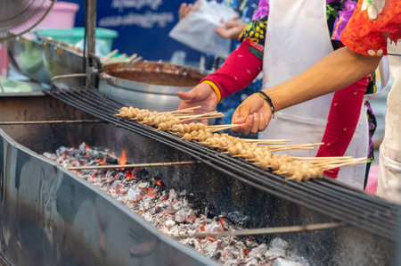 Woman grilled meat ball on charcoal in street food market.の写真素材