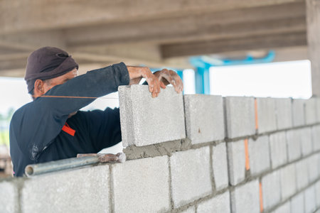 Masonry worker make concrete wall by cement block and plaster at building siteの写真素材
