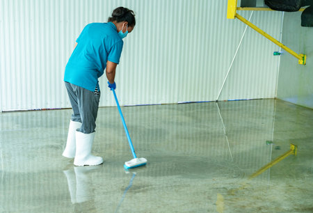 Worker cleaning cement floor with long brush in factoryの写真素材