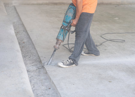 Worker at construction site demolishing concrete floor with electric plugger hammer.