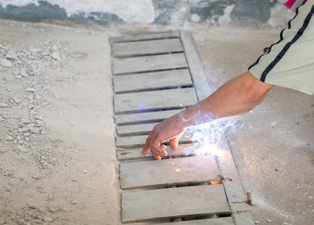 Worker welding stainless steel grill of drain rail on floor.
