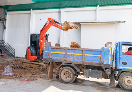 Mini excuvator unloading soil with truck in construction site.