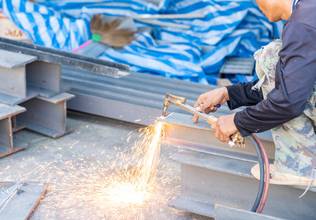 Worker cutting beam with an industrial gas cutter in factory workshop.