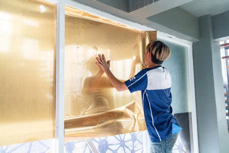 Tinted glass in the building. window dimming by golden dimness film. hands apply tint film to the window.の写真素材