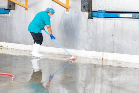 Woman using mop for cleaning floor in factory.の写真素材