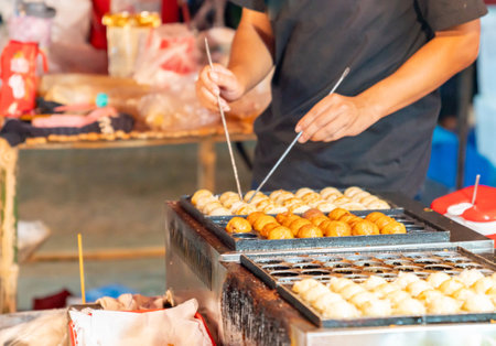 The man is using chopsticks to flip the takoyaki on the hot takoyaki pan at street food market.の写真素材