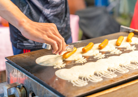 The man paste sausage on dough for make pancake in street food market.の写真素材