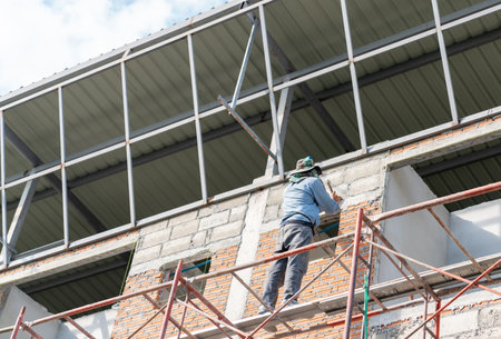The worker is driving nails to create a guide for plastering the wall of the building.