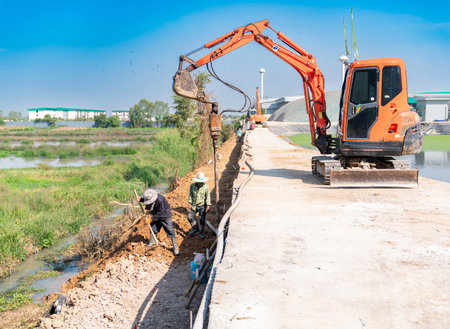 The workers are clearing the area around the hole that the small excavator has dug.の写真素材