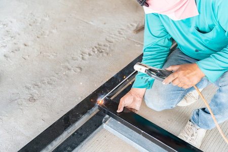 Worker is welding galvanized steel pipe for improvement building structure at workshop in...