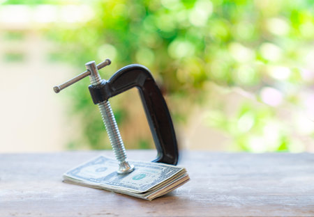 Dollar bills pinched by a C clamp concept of Financial pressure or Financial strain.