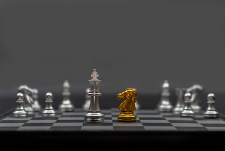 Gold horse chess and silver king chess encounter on a chessboard in the dark background.の写真素材