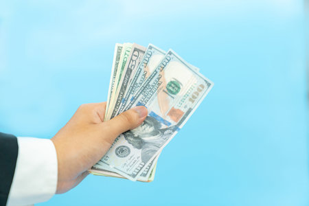 Close up dollar bills in hand on aqua blue background.