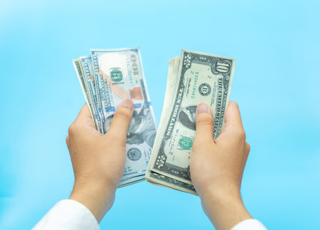 Man hand in white shirt counting dollar banknotes on aqua blue background.