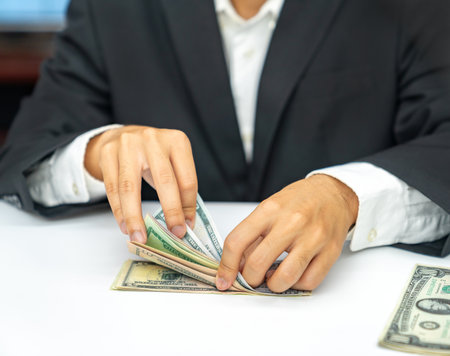 Close up business man countering dollar bills on white table. Concept of business success.の写真素材