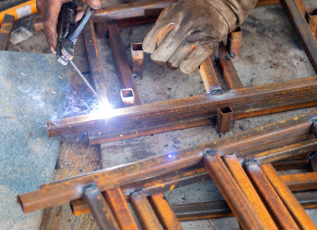 The individual is performing welding on steel at their workplace in the workshop, while the sparks...
